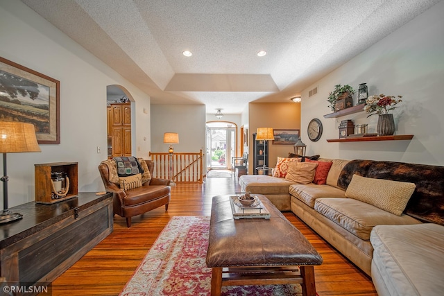 living room featuring a tray ceiling, light hardwood / wood-style flooring, and a textured ceiling