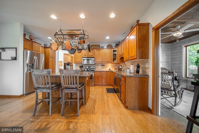 kitchen featuring stone counters, appliances with stainless steel finishes, a center island, light wood-type flooring, and a kitchen bar