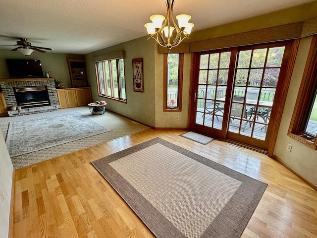 doorway to outside featuring a textured ceiling, a brick fireplace, ceiling fan with notable chandelier, and hardwood / wood-style flooring