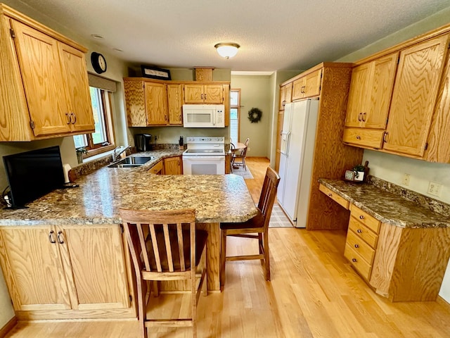 kitchen featuring sink, a kitchen breakfast bar, light hardwood / wood-style flooring, kitchen peninsula, and white appliances