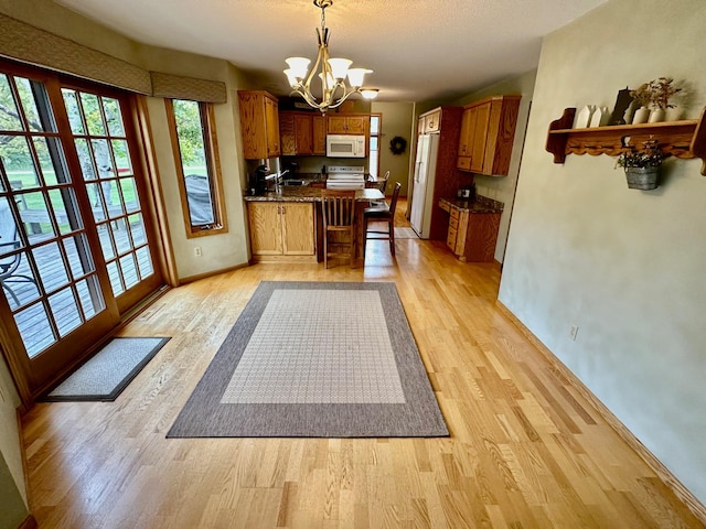 kitchen featuring a notable chandelier, light wood-type flooring, white appliances, and hanging light fixtures