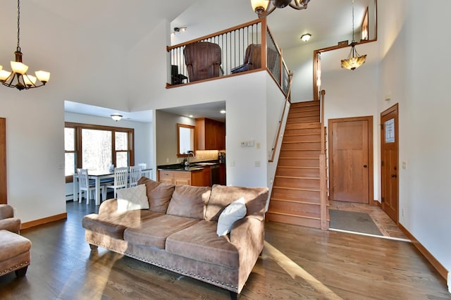 living room featuring sink, a high ceiling, a baseboard radiator, a chandelier, and dark wood-type flooring