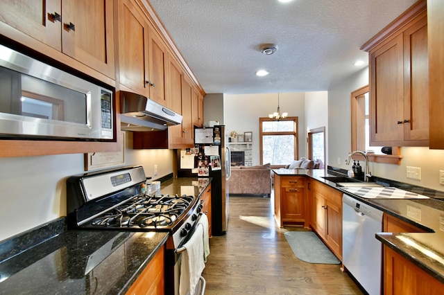 kitchen featuring a stone fireplace, appliances with stainless steel finishes, a notable chandelier, a textured ceiling, and sink