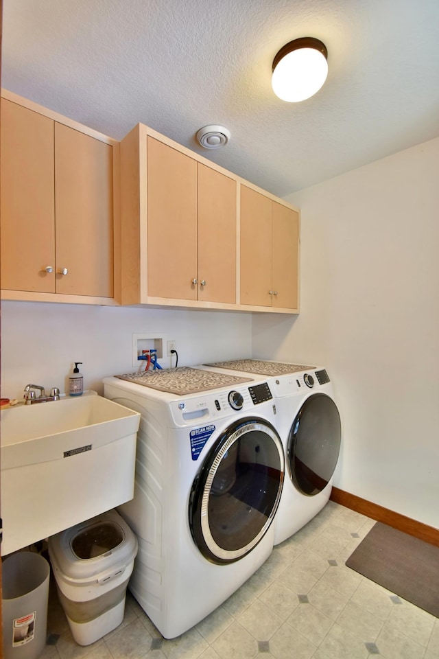 laundry room with a textured ceiling, cabinets, washer and clothes dryer, and sink