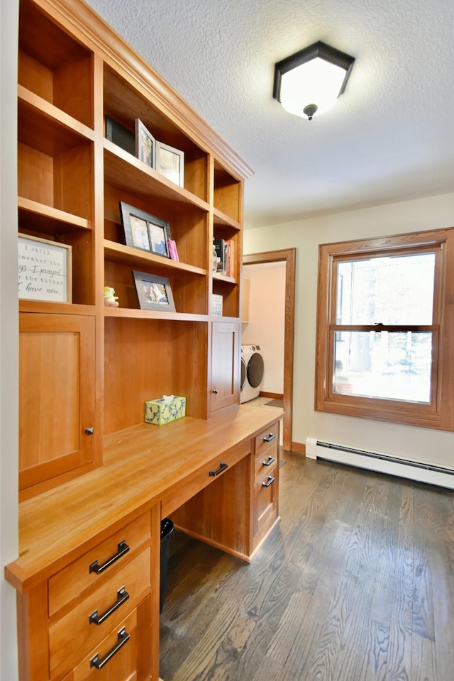 unfurnished office featuring a textured ceiling, dark hardwood / wood-style floors, baseboard heating, washer / clothes dryer, and built in desk