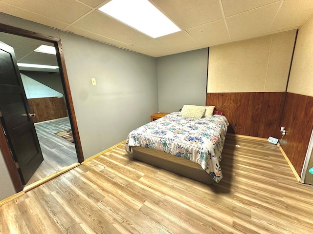 bedroom featuring hardwood / wood-style flooring, wooden walls, and a paneled ceiling