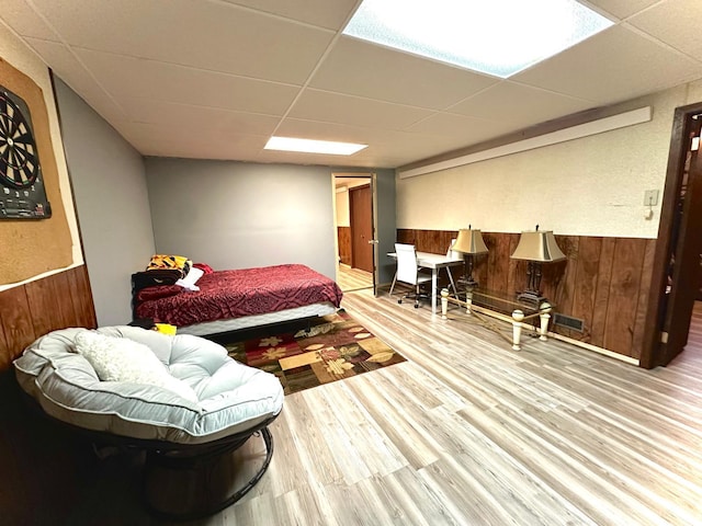 bedroom with wooden walls, a paneled ceiling, and hardwood / wood-style floors