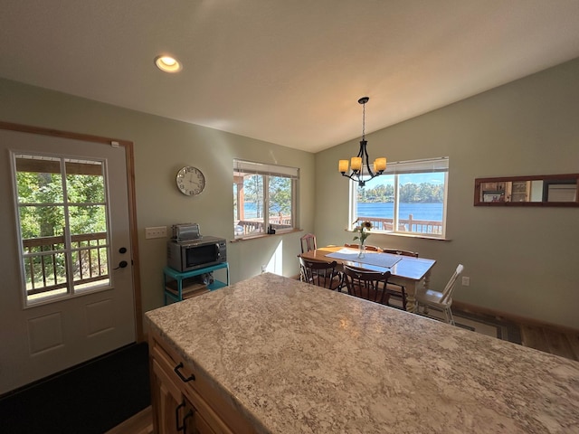 kitchen with hanging light fixtures, a water view, vaulted ceiling, dark wood-type flooring, and an inviting chandelier