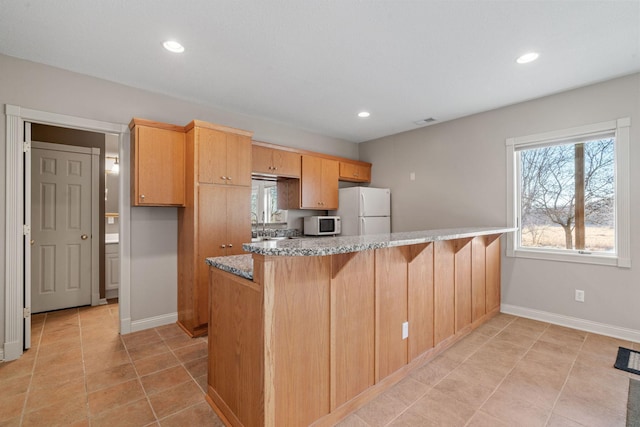 kitchen featuring light tile patterned floors, white appliances, light stone countertops, light brown cabinetry, and kitchen peninsula