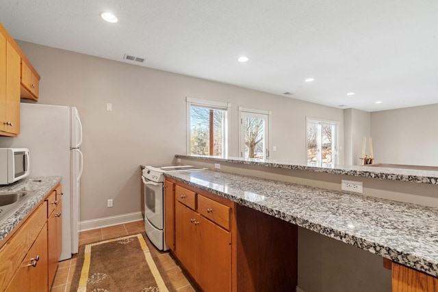 kitchen with light tile patterned flooring, light stone countertops, sink, and white appliances