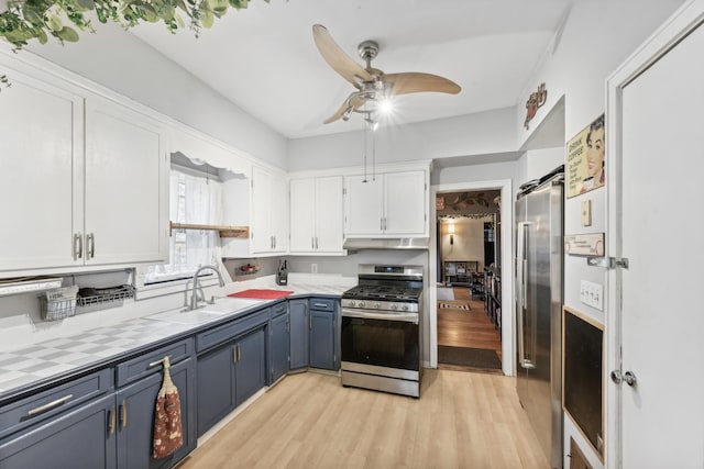 kitchen with sink, light wood-type flooring, blue cabinetry, appliances with stainless steel finishes, and white cabinetry