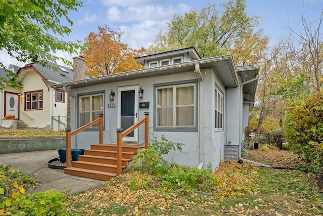 bungalow-style house with entry steps, a chimney, and stucco siding