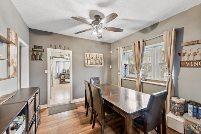 dining space with light wood finished floors, baseboards, a ceiling fan, and a textured ceiling