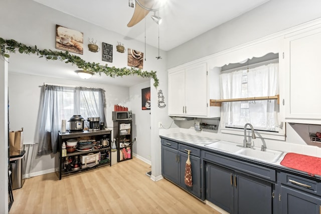 kitchen featuring light wood-style floors, stainless steel microwave, white cabinets, and a sink