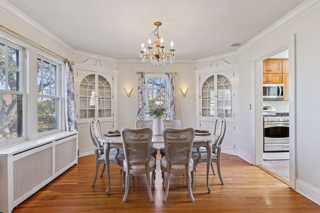 dining room featuring radiator heating unit, a chandelier, ornamental molding, light wood-type flooring, and a textured ceiling