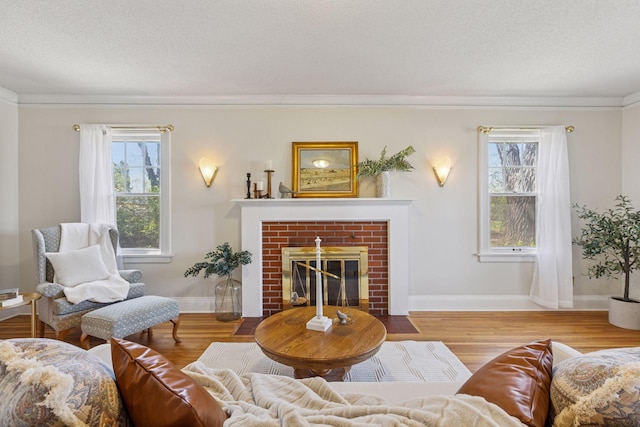 living area with crown molding, wood finished floors, a fireplace, baseboards, and a textured ceiling