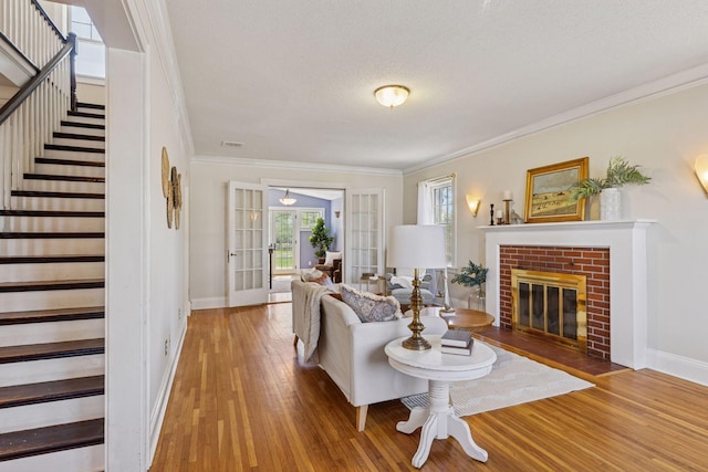 living room with stairway, baseboards, wood finished floors, crown molding, and a brick fireplace