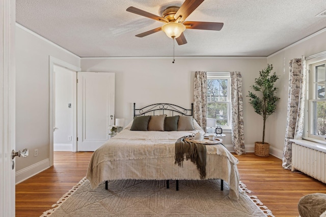 bedroom with radiator heating unit, multiple windows, wood finished floors, a textured ceiling, and ornamental molding