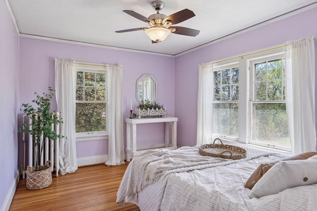 bedroom with baseboards, multiple windows, wood finished floors, ceiling fan, and ornamental molding