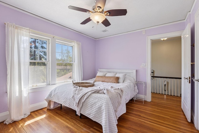 bedroom with wood finished floors, baseboards, a ceiling fan, and crown molding