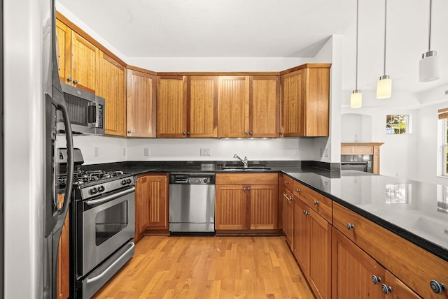 kitchen featuring sink, light hardwood / wood-style floors, stainless steel appliances, decorative light fixtures, and dark stone countertops