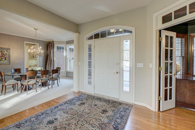 foyer entrance featuring ornate columns, a notable chandelier, and light hardwood / wood-style flooring