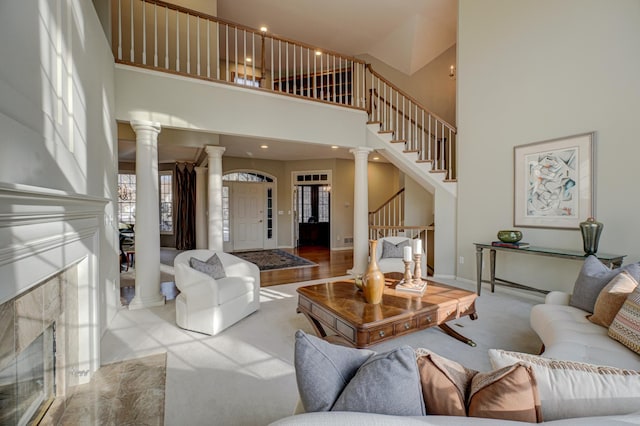 carpeted living room featuring a towering ceiling, a fireplace, and ornate columns