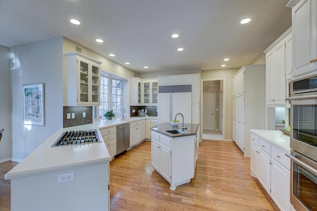 kitchen featuring stainless steel appliances, sink, white cabinets, an island with sink, and decorative backsplash