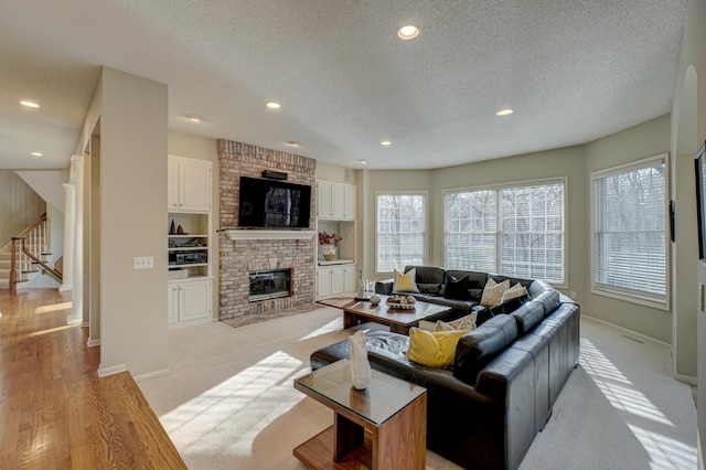 living room with a textured ceiling, a healthy amount of sunlight, a fireplace, and light hardwood / wood-style flooring