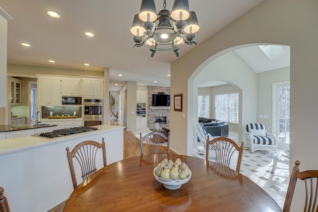 dining area featuring sink, a brick fireplace, vaulted ceiling, and a chandelier