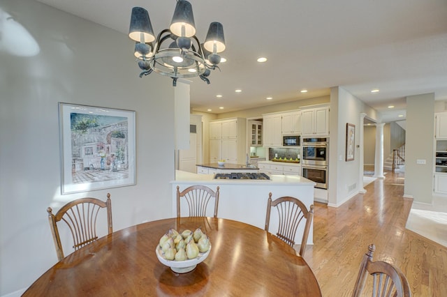 dining room featuring an inviting chandelier, decorative columns, and light wood-type flooring