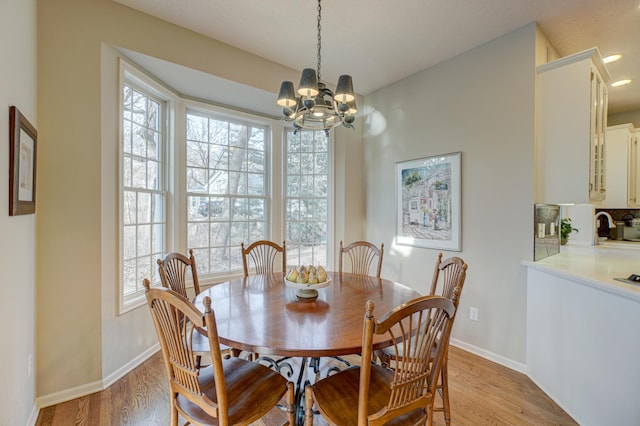 dining space featuring sink, light wood-type flooring, and an inviting chandelier