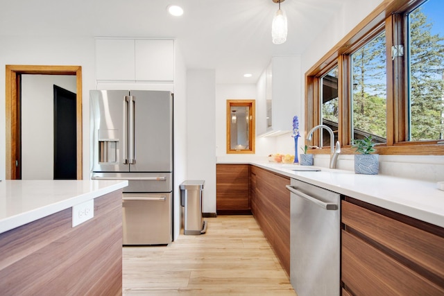 kitchen with white cabinetry, stainless steel appliances, light wood-type flooring, decorative light fixtures, and sink