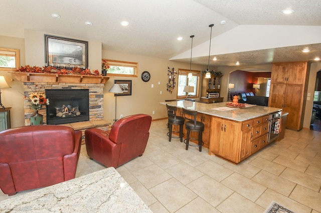 kitchen with lofted ceiling, decorative light fixtures, a kitchen island, a stone fireplace, and a kitchen bar