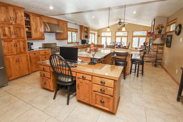 kitchen with lofted ceiling, pendant lighting, a kitchen island, wall chimney range hood, and a breakfast bar area