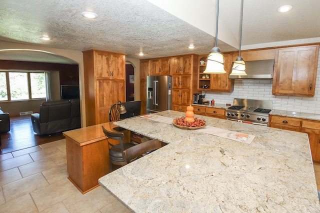 kitchen with a center island, light stone countertops, wall chimney range hood, premium appliances, and pendant lighting