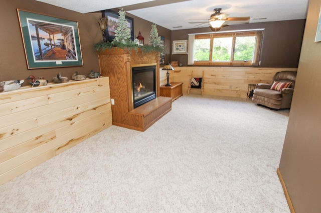 carpeted living room with wooden walls and ceiling fan