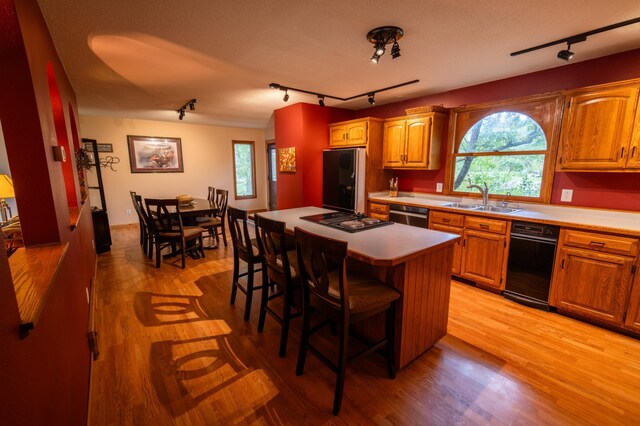 kitchen with a kitchen breakfast bar, light hardwood / wood-style floors, stainless steel appliances, a center island, and sink