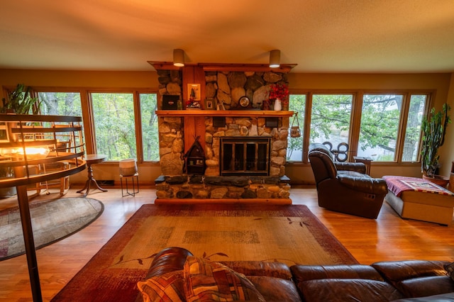 living room featuring a healthy amount of sunlight, a stone fireplace, and hardwood / wood-style floors