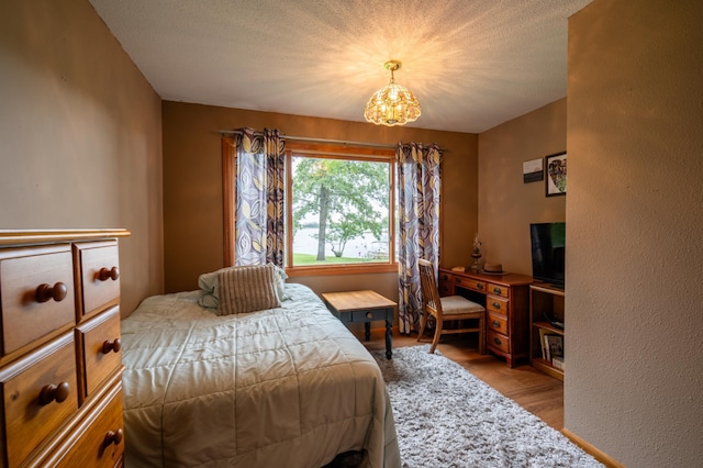 bedroom featuring light wood-type flooring, a textured ceiling, and a chandelier