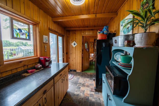 kitchen with black refrigerator, wooden walls, beamed ceiling, and plenty of natural light