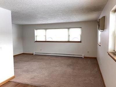 carpeted empty room featuring a textured ceiling and baseboard heating