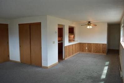 interior space featuring carpet flooring, wooden walls, and ceiling fan