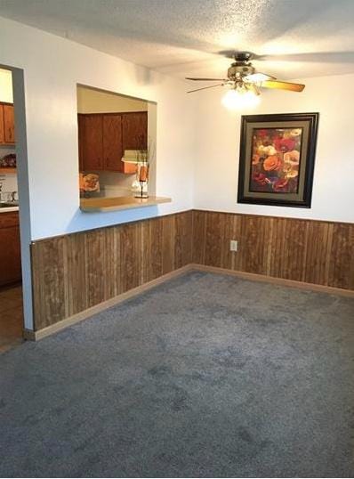 spare room with carpet floors, a textured ceiling, wooden walls, and ceiling fan