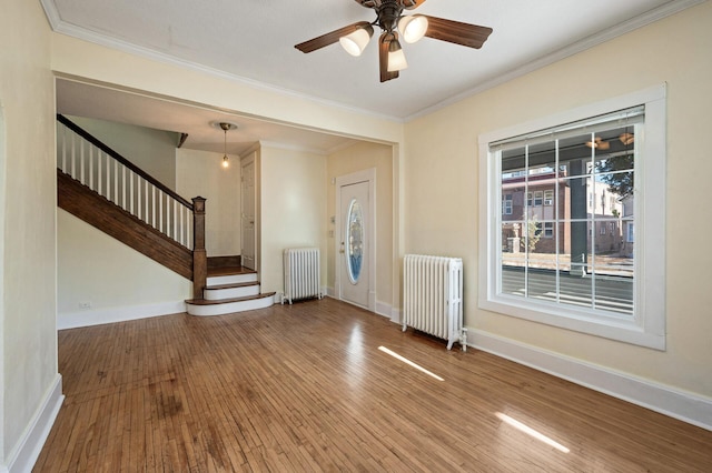 entryway with ornamental molding, radiator heating unit, wood-type flooring, and ceiling fan