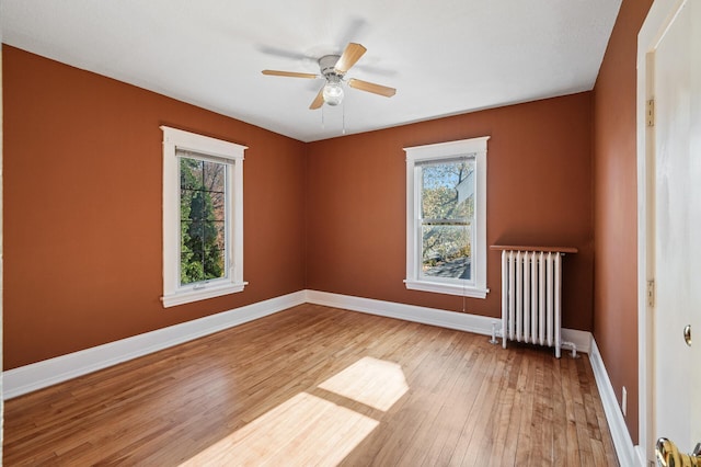 unfurnished room featuring a wealth of natural light, ceiling fan, radiator heating unit, and hardwood / wood-style flooring