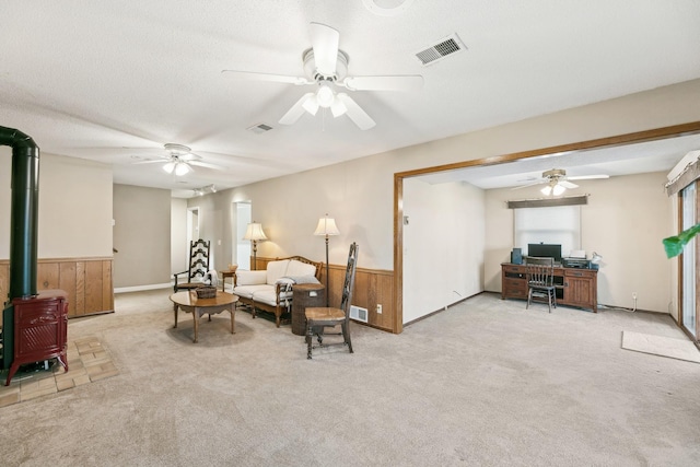 sitting room featuring a textured ceiling, wooden walls, light carpet, and a wood stove