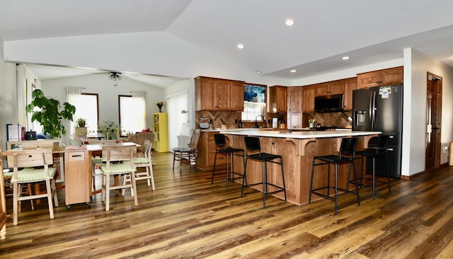 kitchen featuring stainless steel fridge, lofted ceiling, dark hardwood / wood-style floors, and a kitchen breakfast bar