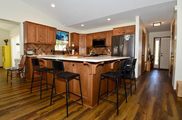 kitchen featuring tasteful backsplash, dark hardwood / wood-style flooring, vaulted ceiling, stainless steel appliances, and a kitchen bar