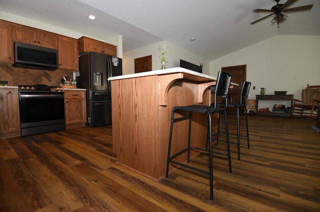 kitchen featuring ceiling fan, stainless steel appliances, dark hardwood / wood-style flooring, vaulted ceiling, and a kitchen bar